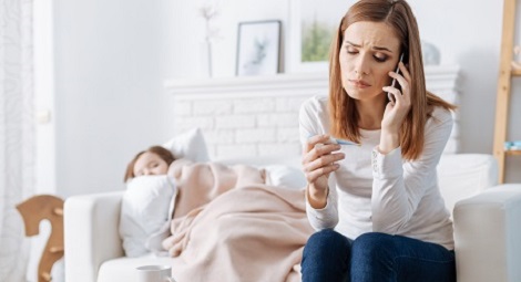 Mother on phone looking concerned with a child asleep in the background